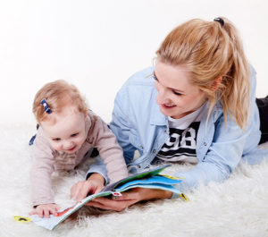 young woman and baby girl laying on a rug reading a book together